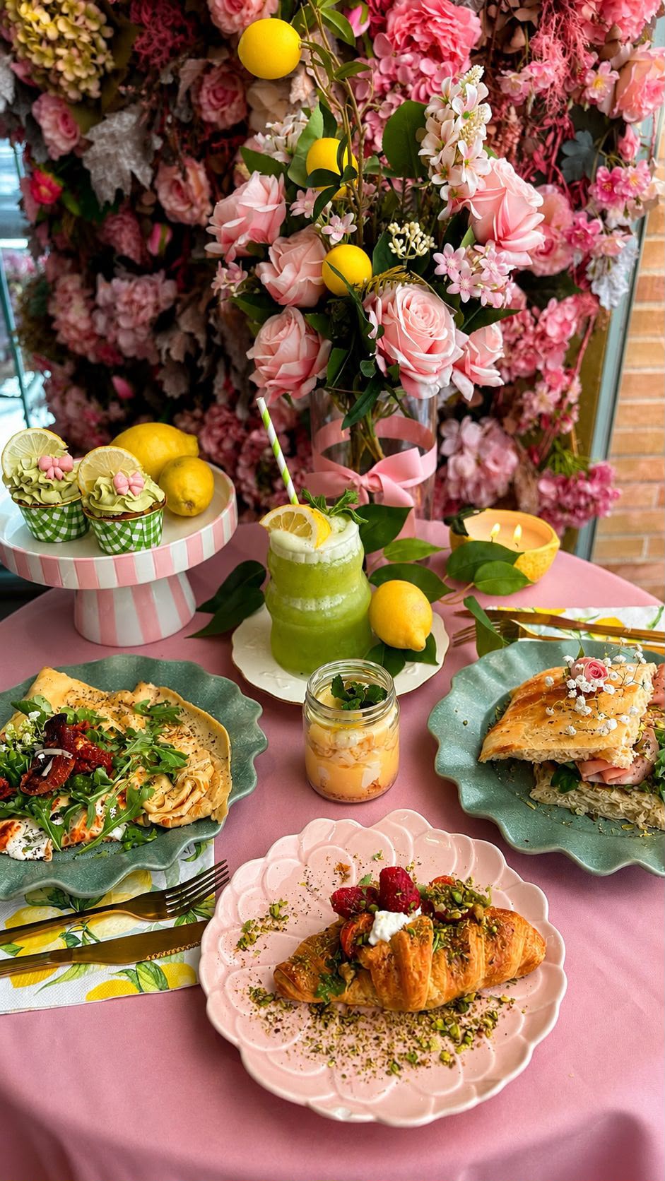 Mesa de brunch con croissant, crepe y focaccia entre flores y limones